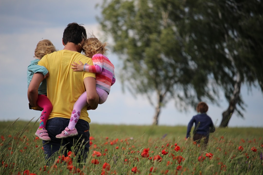 A parent carrying two children through a field